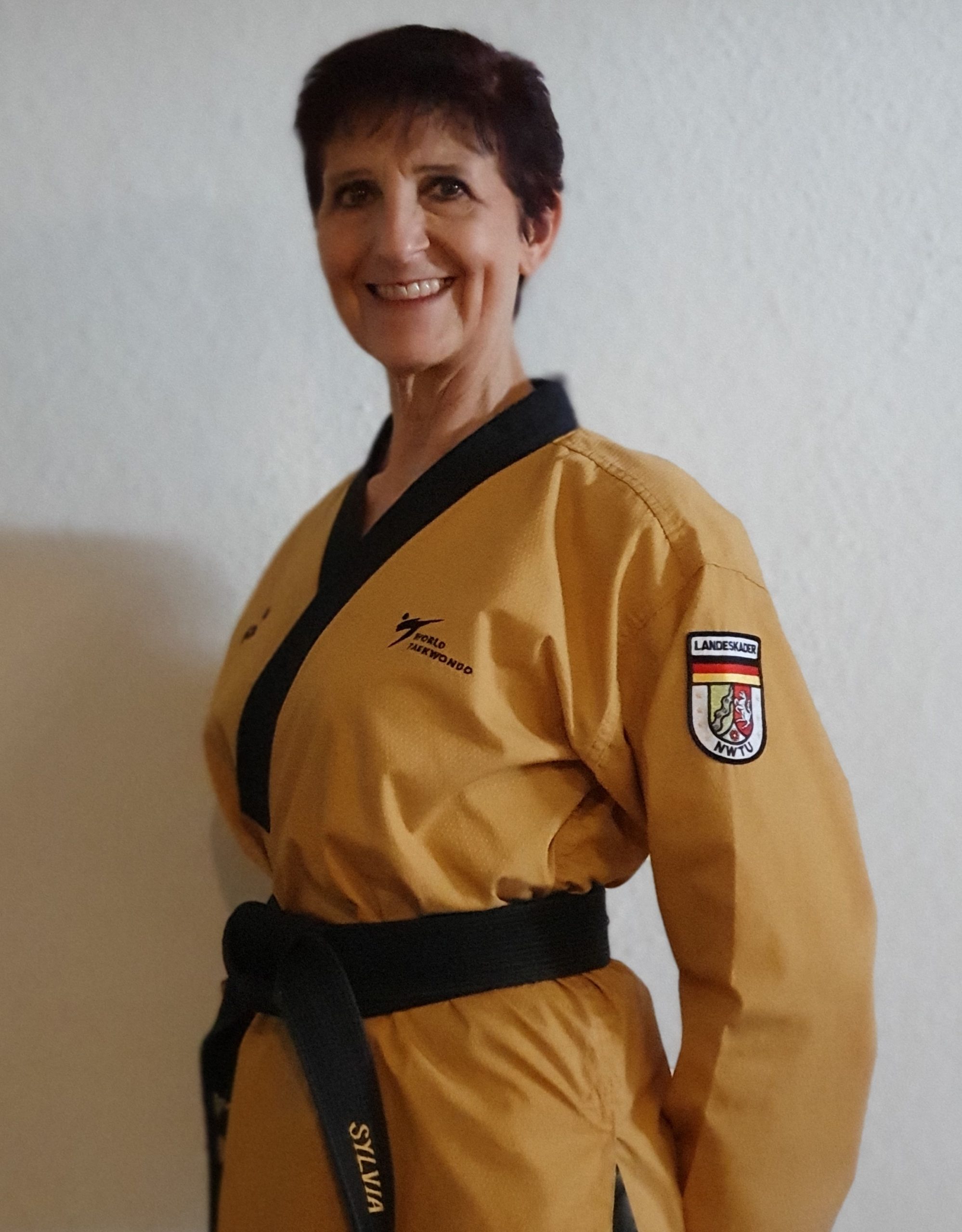 Eine Frau im goldfarbenen Taekwondo-Dobok steht seitlich zur Kamera und lächelt.