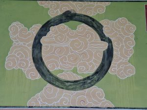 Gemaltes Wolkenmotiv mit großem schwarzen Kreis auf grünem Hintergrund.