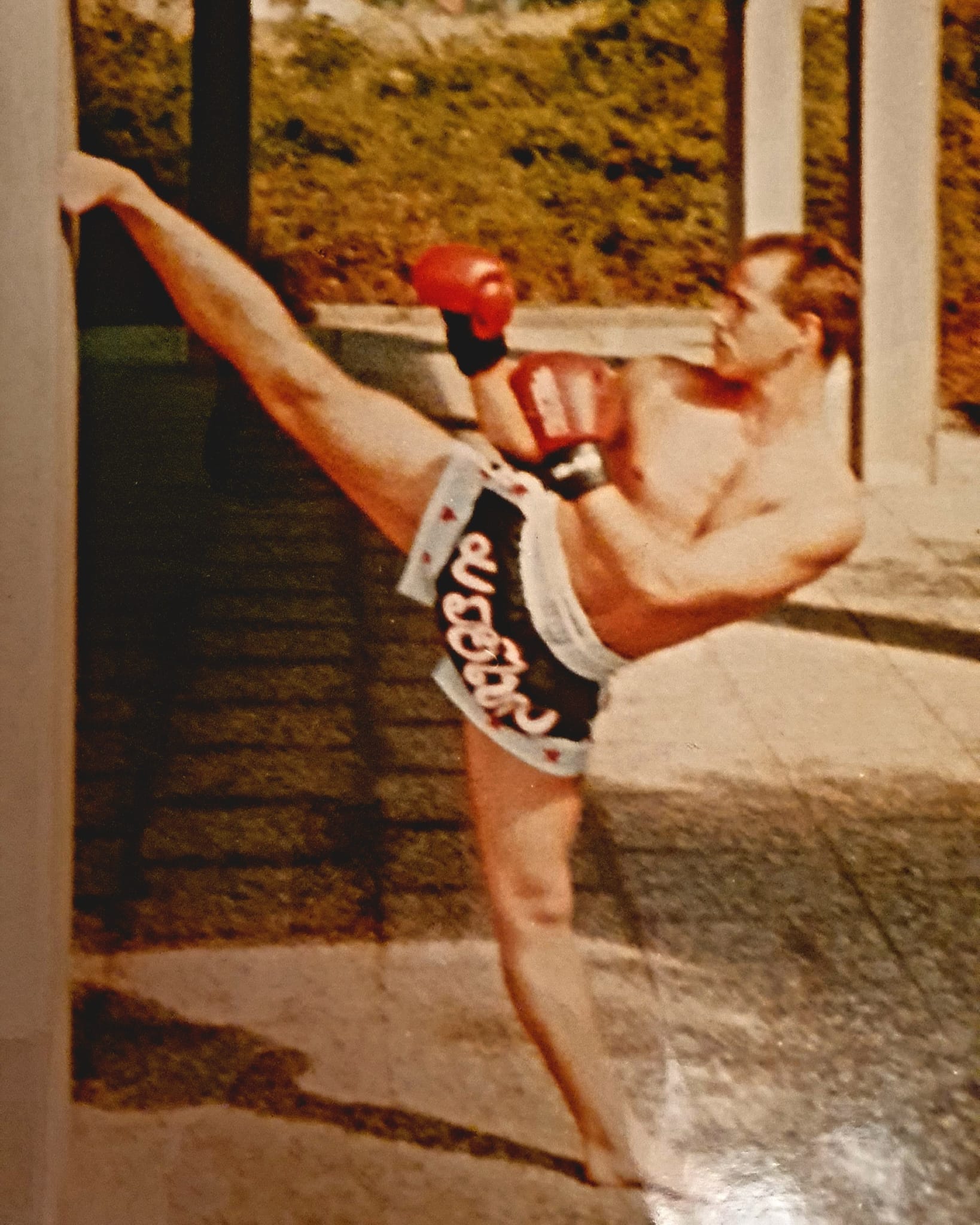Rainer Denschlag führt einen hohen Seitkick aus und stützt das Bein an einer Wand. Er trägt Boxhandschuhe.