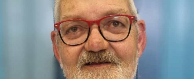 Porträt eines älteren Mannes mit Brille, Bart und hellem Sakko.