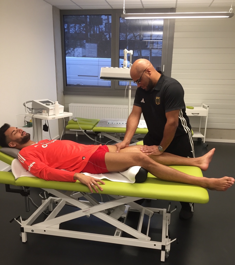Ein Physiotherapeut behandelt in einer Praxis einen Sportler, der auf einer Liege liegt.