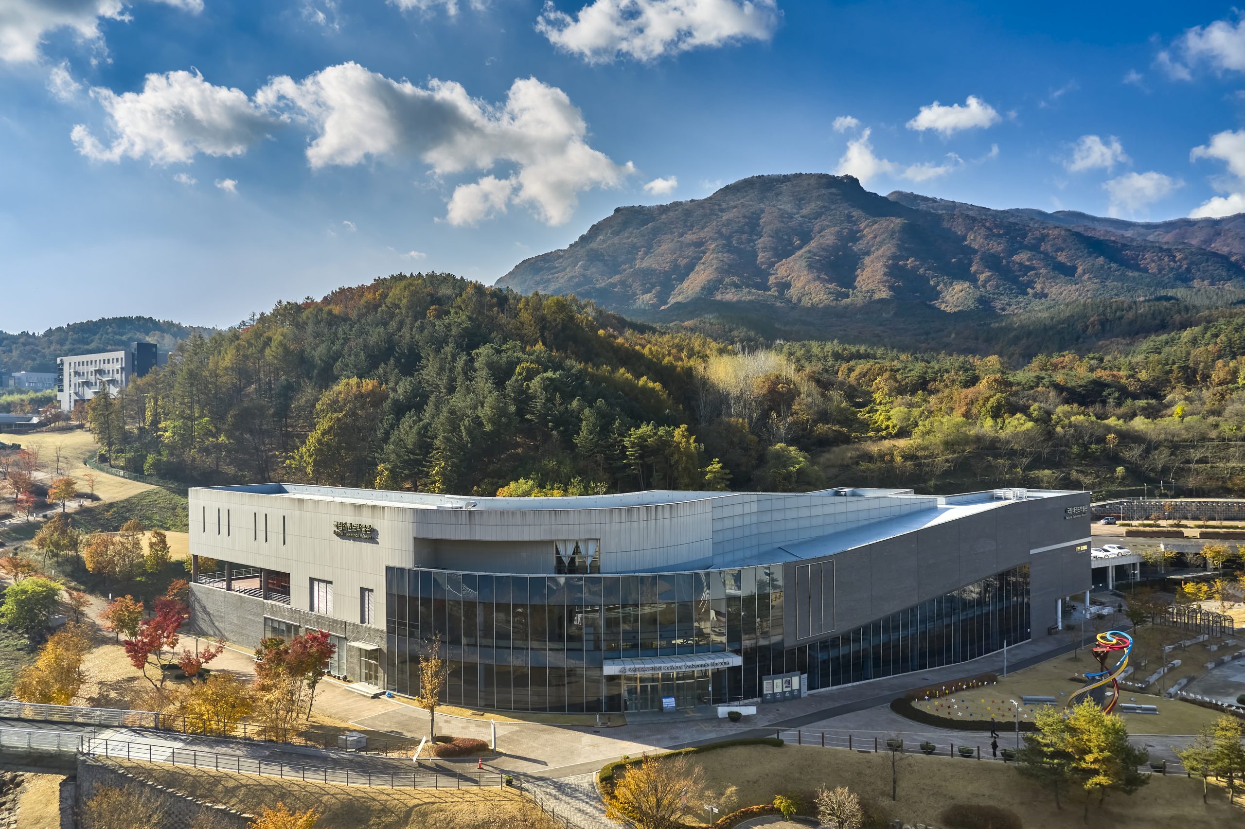 Modernes Gebäude des National Taekwondo Museums vor einer herbstlichen Berglandschaft.