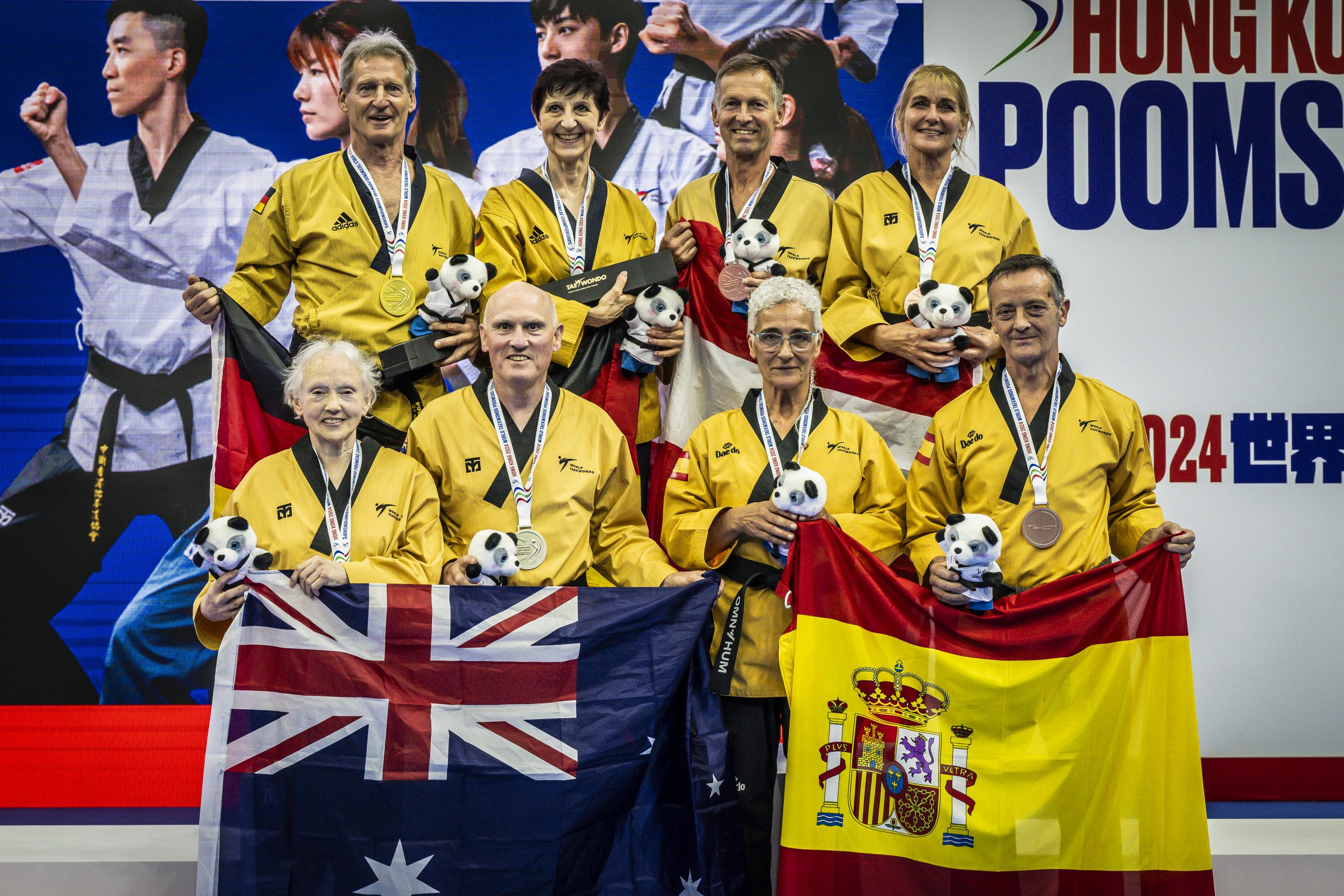 Eine Gruppe internationaler Taekwondo-Sportlerinnen und -Sportler steht auf dem Siegerpodest und präsentiert ihre Medaillen.